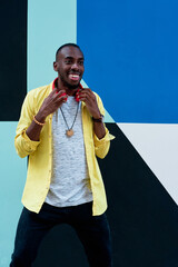 black guy in yellow shirt and red headphones laughing standing next to a colorful wall