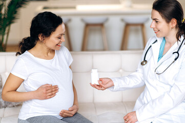 Healthy pregnancy concept. A doctor prescribes medications or vitamins to a happy mixed race pregnant woman, sitting on a sofa at the doctor's appointment, at home or in the hospital