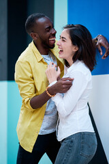 couple of young multiethnic men standing and hugging next to a very colorful wall, black boy and white girl in love,