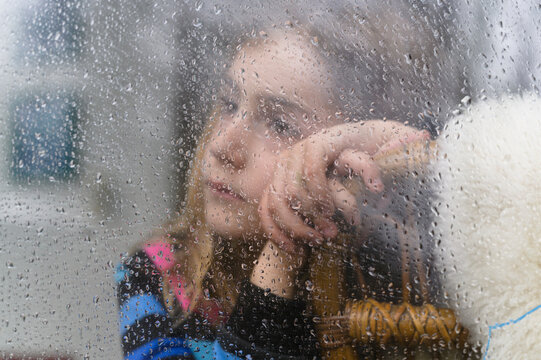 Close-up of girl (8-9) looking through window on rainy day