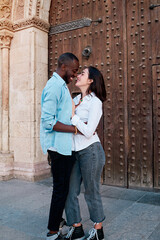 couple of young multiethnic guys kissing and laughing in front of the door of a cathedral, black guy and white girl in love