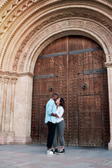 couple of young multiethnic guys kissing and laughing in front of the door of a cathedral, black guy and white girl in love