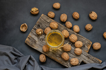 Glass jar of walnut oil with dry walnuts on rustic table