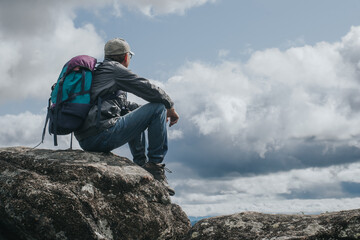Tourist with backpack sits on the top of the mountain,resting and admiring the view from...