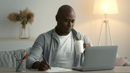 African Man Taking Notes Having Coffee Sitting At Laptop Indoor