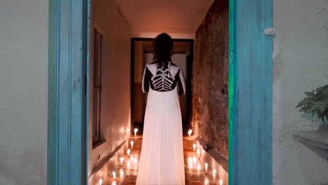 Hispanic woman in a performance for the day of the death in Mexico with burning candles walking a corridor. Body paint of a skeleton for a mexican celebration. 4k