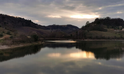 Fototapeta na wymiar Verdi colline dell’Appennino marchigiano si riflettono al tramonto nelle acque del lago
