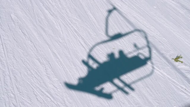Shadow in the snow from the chair lift with a skier and snowboarder along a mountain ski run