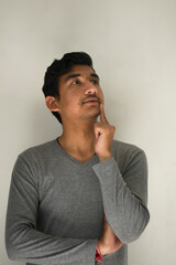Indian boy thinking about something and hand on cheek, wearing light grey full sleeves t-shirt in isolated white background