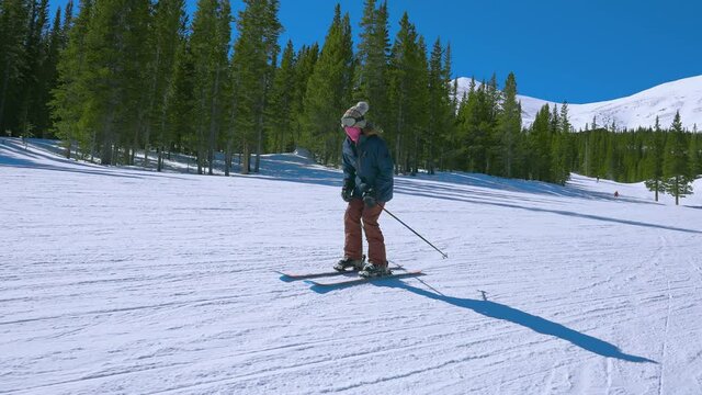 Panning around a Female Downhill Skier as she Skies Down a Bunny Hill with large mountains in the distance