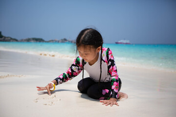 Asian girl in a floral dress is sitting on the beach.