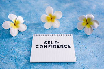 positive attitude concept, Self-confidence text on notepad with tropical flowers around it
