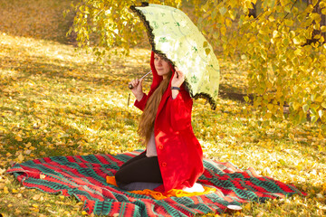 Fototapeta na wymiar Sexy girl in a red coat with long hair in an autumn park holding an umbrella