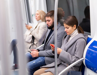 Fototapeta na wymiar Young woman absorbed in her smartphone while traveling in subway car..