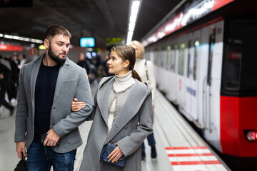 Young bearded man with his girlfriend wearing light overcoats walking on modern underground station