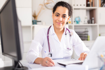 Portrait of female doctor who is working with laptop and documents