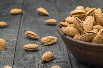 Shelled almonds on a black wooden table in a clay bowl.