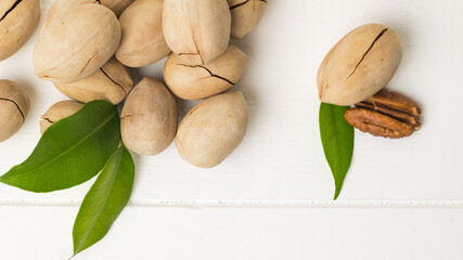 Pecans and green leaves on a white wooden table.