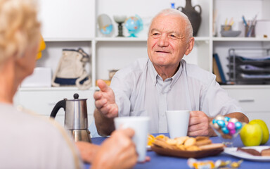 Smiling elderly man enjoying time at home, drinking tea and talking with woman