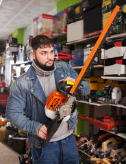 Portrait of yung man with an electric brush cutter in hardware store