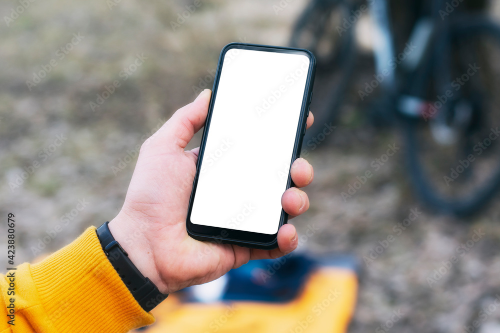 Poster a man cyclist holds a mock-up of a smartphone with a white screen in his hands on the background of 