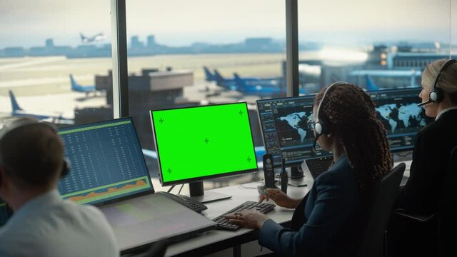 Female Air Traffic Controller with Headset Works on Computer with Green Screen Mock Up in Airport Tower. Office Room with Displays with Navigation Screens, Airplane Flight Radar Data for the Team.