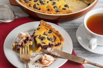 Fresh slice of cherry pie with ice cream and white cup with tea on a wooden background