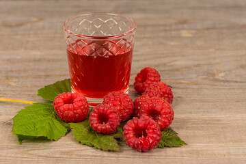 homemade sweet raspberry wine or juice in small glasses with fresh berries on aged wooden table