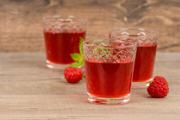 homemade sweet raspberry wine or juice in small glasses with fresh berries on aged wooden table