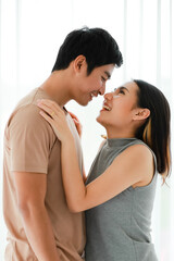 Portrait shot of cute smiling young Asian lover couple standing and passionate kissing together in the bedroom at weekends. Boyfriend and girlfriend sharing an intimate loving moment at home