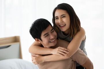 Portrait shot of cute smiling young Asian lover couple in casual clothes cuddle on white background. The wife stands behind her husband and embracing him with love