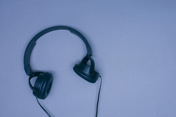 Large black musical headphones with a wire on a gray background.