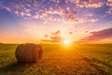 Sunset in a field with haystacks on a summer or early autumn evening with a cloudy sky in the...