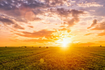 Sunset in a field with haystacks on a summer or early autumn evening with a cloudy sky in the...