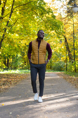 Fototapeta premium Cheerful african american young man in stylish clothes walks in autumn park on sunny warm autumn day. Concept of weekend and outdoor recreation