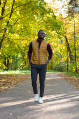 Cheerful african american young man in stylish clothes walks in autumn park on sunny warm autumn day. Concept of weekend and outdoor recreation