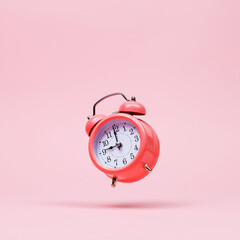 The pink alarm clock is levitate in the air, against a pink background. The concept of time, copy...
