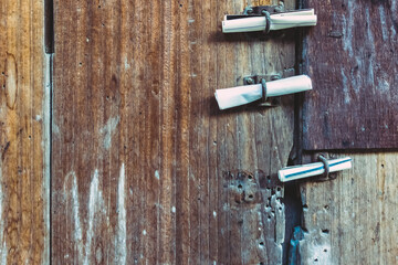 Three small rolls of white papers notification inserted into old rusty padlock hasp on the old wooden door. Bulletin sticking out at the gate of the abandoned house. Selective focus.