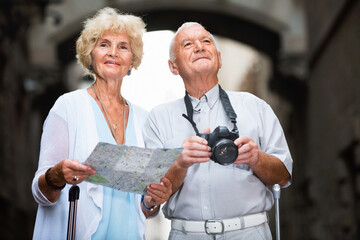 Pleasant smiling senior man photographing sights while his wife looking map near old cathedral