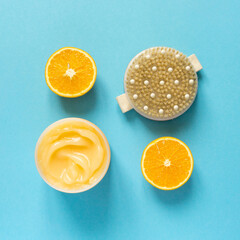 Orange anti-cellulite cream and brush for dry massage on blue background, top view