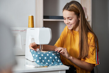 Cheerful girl seamstresses sewing clothes in workshop
