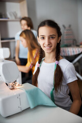 Cute joyful girl sewing clothes in workshop