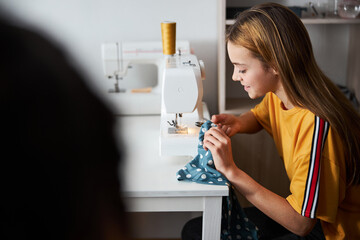 Charming girl seamstress sewing clothes in workshop