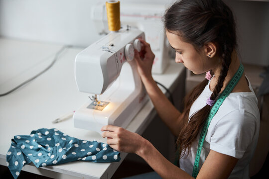 Adorable girl seamstress sewing clothes in workshop