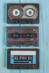 Three audio cassettes in black cases lie on a blue wooden background