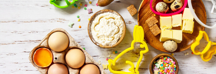 Baking or cooking background frame. Ingredients, kitchen items for Easter festive baking. Kitchen utensils, flour, brown sugar, eggs, butter, confetti on rustic kitchen table. Flat lay. Banner.