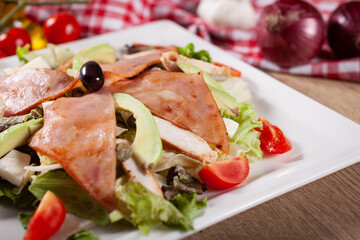 Fototapeta na wymiar Green salad with avocado, arugula, capers, cherry tomatoes, mozzarella and baked ham