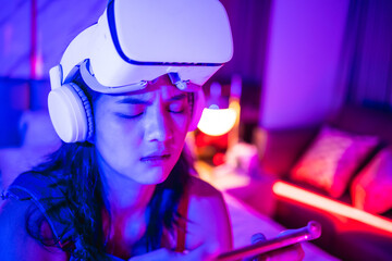 Young asian woman is using virtual reality headset. Neon light studio portrait. Concept of virtual reality, simulation, gaming and future technology.Asian woman play game in bedroom.