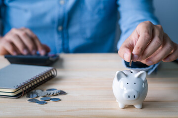 close up  businessman holding coins putting in piggy bank and using calculator. concept saving...