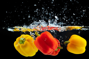 Bell pepper falling into water with a splash against black background